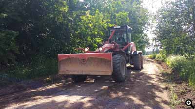 Ein Grader profiliert einen Hauptweg. Vorne ist das Frontschild, welches auch Planierschild genannt wird.